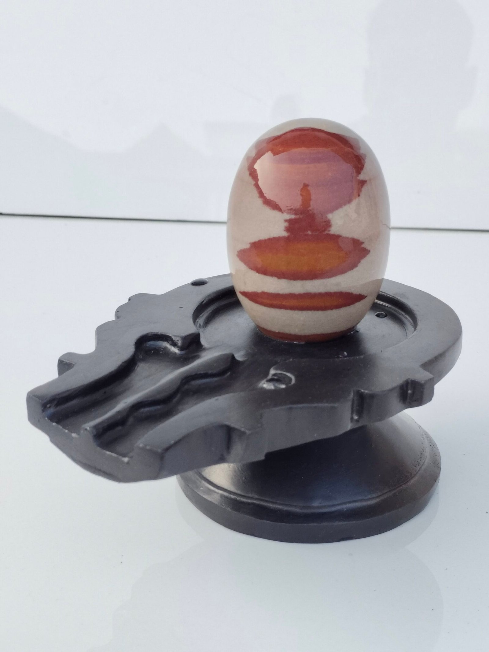 A smooth, oval-shaped Narmadeshwar Shivling with brown and beige horizontal bands, resting on a black stone jaladhari base.