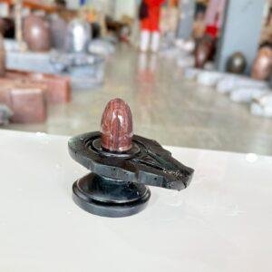 A polished, red-veined Narmadeshwar Shivling stone set upright on a smooth, black circular yoni base.