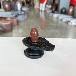 A polished brown stone Shivling with natural patterns sits centered on a black stone Yoni base.